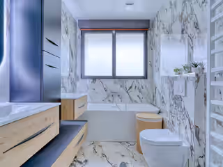 La même salle de bain refaite : carreaux effet marbre, meuble vasque en bois clair, baignoire neuve sous la fenêtre