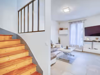 Le même séjour : escalier bois vernis, verrière noire au-dessus, murs blancs, carrelage clair