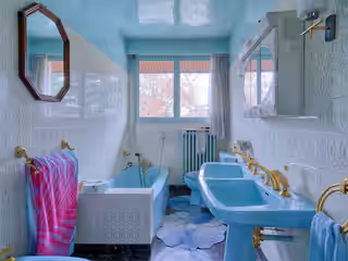 Ancienne salle de bain : baignoire et lavabos bleu ciel, carrelage à motifs, robinetterie dorée
