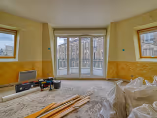 Séjour d’appartement en travaux : murs jaunes tachés, sol à nu, gravats en sacs