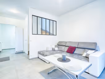 Séjour lumineux, verrière noire en haut du mur, canapé gris et table basse