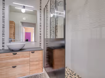 Salle d’eau : vasque posée sur un meuble en bois, douche vitrée, carreaux blancs