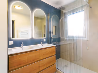 Salle de bain : double vasque sur meuble bois, miroirs arrondis éclairés, faïence bleue
