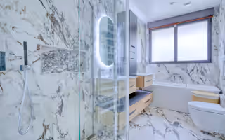 Salle de bain refaite en grands carreaux effet marbre, douche vitrée, miroir rétroéclairé, baignoire sous la fenêtre